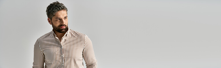 Obraz premium A stylish man with an alluring beard poses confidently in elegant attire against a sleek white backdrop.