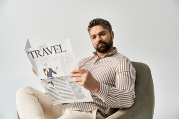 A stylish man with a beard sitting in a chair engrossed in reading a newspaper, exuding...