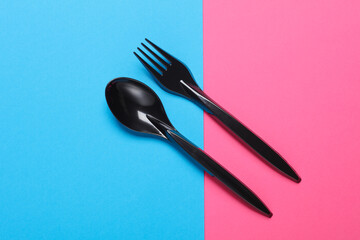 Black plastic spoon and fork on pink blue background