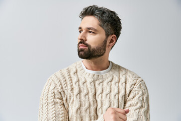 A charismatic man with a beard strikes a pose in a white sweater against a grey studio background.