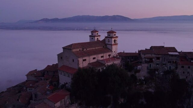 Aerial view of Santo Stefano church at sunrise with fog and mountain backdrop, Artena, Italy.