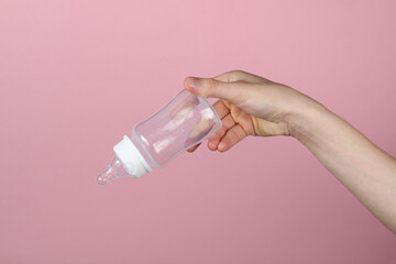 Woman's hand holds bottle with nipple for feeding newborn on a pink background