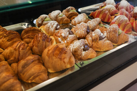 Cornetti artigianali vuoti, ripieni di cioccolato, marmellata e frutti di bosco esposti nella vetrina di un bar e pronti per essere venduti per colazione