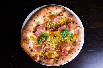 Pizza tradizionale gourmet napoletana con mozzarella, prosciutto crudo pomodori gialli, pesto di pistacchio, granella di pistacchio e basilico fresco servita in una pizzeria