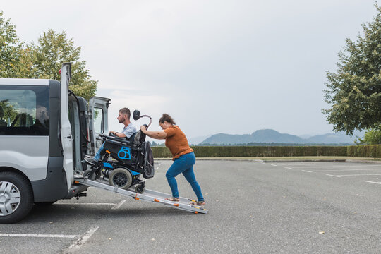 Man with a disability, a wheelchair user getting into an accessible vehicle, with the help of his girlfriend and a ramp for transportation.