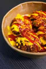 Polpette fritte guarnite con cheddar fuso e salsa bbq e condite con pancetta croccante servite in un contenitore di cartone per i cibi d'asporto