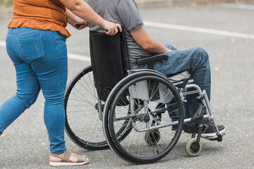 Obraz premium Personal assistant helping a man with disability to push a wheelchair outdoors. Help service concept.