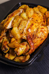 Pollo allo spiedo con contorno di patate al forno servito in un contenitore di plastica nero per...
