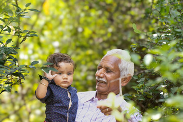 Grandfather Holding indian Grandchild in Garden Looking at Camera