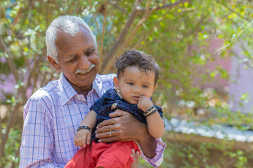 Grandfather Smiling While Holding indian Grandchild in a Park