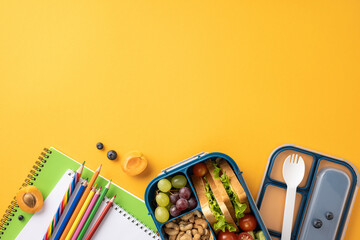 Top view of a healthy school snack with a lunchbox, notebooks, and pencils on a vibrant yellow...