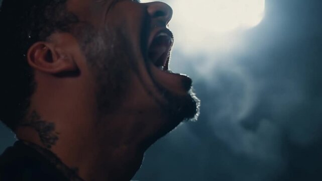 This man with a tattoo yells with a wide-open mouth. Emotion despair