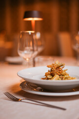 Piatto di rigatoni con carciofi fritti croccanti, fiori di zucca e pancetta croccante servito come...