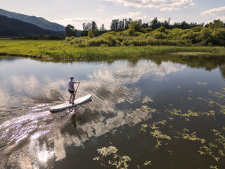 Woman paddling a white stand up paddle board exploring the lakeshore and enjoying a fantastic...