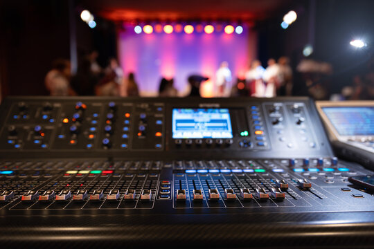 Live theater concert show sound video music control console with scene lights background. Sound engineer mixer soundboard equipment with many knobs, buttons, faders, equalizer screen and light