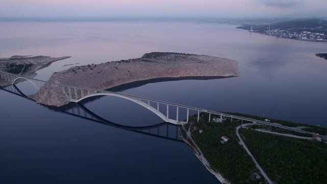 Aerial view of serene coast with arch bridge and reflection in the Adriatic Sea, Krk, Croatia.