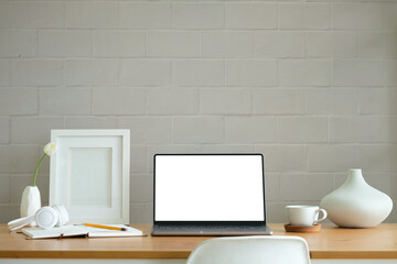 Workplace comfortable with computer laptop, coffee cup, notebook, picture frame and flower pot.