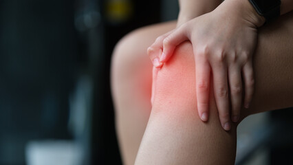 Close up image of female athlete feeling pain and holding her injured knee during exercise at the...