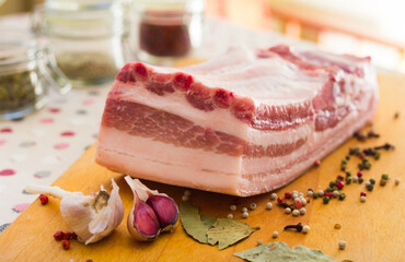 Fresh piece of pork belly on wooden board with spices