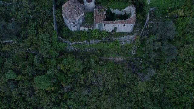 Aerial view of ancient church ruins surrounded by overgrown forest and majestic mountains, Prcanj, Kotor Bay, Montenegro.