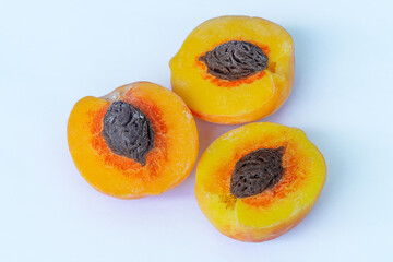 Three longitudinally cut pieces of a peach with a textured dark brown seed isolated on a white background with shadows. Blank for artwork