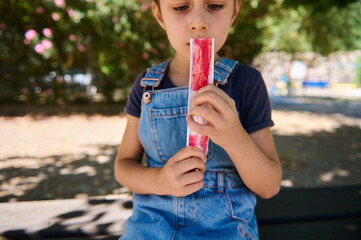 Child enjoying a red popsicle on a sunny day at the park