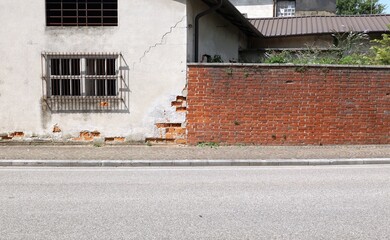 Old abandoned industrial building with peeled facade and surrounding brick wall at the roadside. Sidewalk and street in front. Background for copy space.