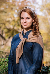 woman long curly red hair wearing blue denim shirt brown sweater draped over her shoulders. smiling...