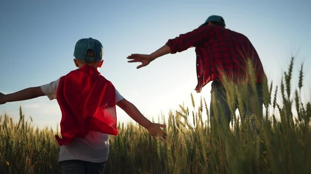 Father and son in field. Family playing together at sunset. Boy superhero cape. family time. Son play hero with dad. Family bonding moment. Superhero adventures in nature. Family play superhero game.