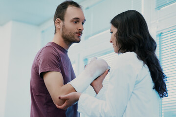 Fototapeta premium Doctor examining male patient with broken arm in plaster cast