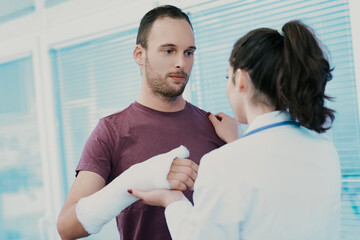 Obraz premium Doctor examining male patient with broken arm in hospital room