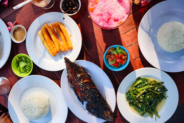 Rice, grilled fish, vegetables and chili sauce as well as various dishes on the table. Asian food