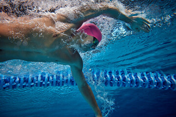 Image of male swimmer in action, demonstrating perfect form and technique, as he glides through pool, wearing blue swim trunks and goggles. Concept of professional sport, competition, motion.