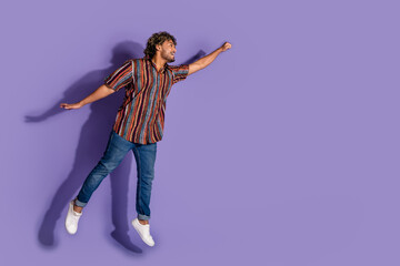 Full size photo of positive man dressed print shirt jeans flying empty space raising fist look at sale isolated on purple color background