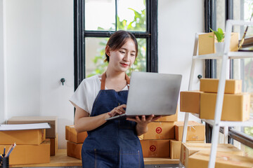 Portrait business woman smile and use laptop checking information on parcel shipping box before send to customer. Entrepreneur small business working at home. SME business online marketing.