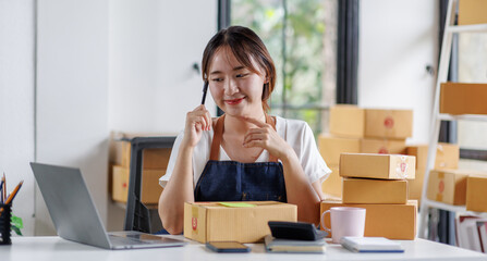 Portrait business woman smile and use laptop checking information on parcel shipping box before send to customer. Entrepreneur small business working at home. SME business online marketing.