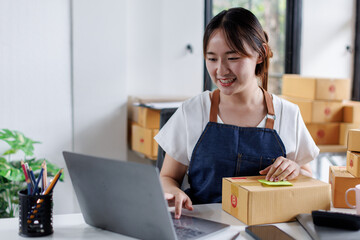 Portrait business woman smile and use laptop checking information on parcel shipping box before send to customer. Entrepreneur small business working at home. SME business online marketing.