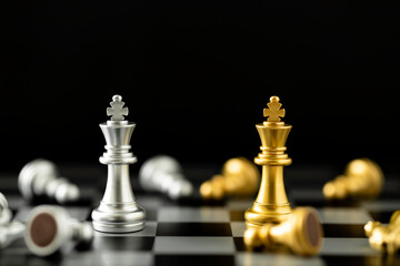 The Golden and silver king chess piece standing on chessboard in front of pawn chess pieces on Black background.