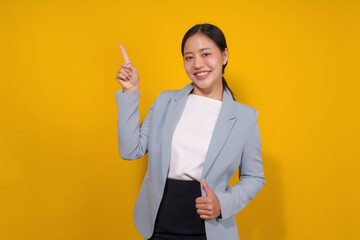 Confident young asian businesswoman in blue blazer pointing up with bright idea, against yellow...