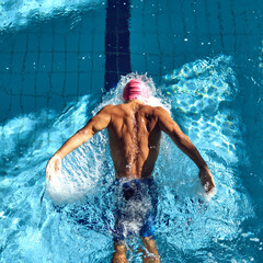 Overhead view swimmer in pink cap performs powerful butterfly stroke, his back muscles rippling...