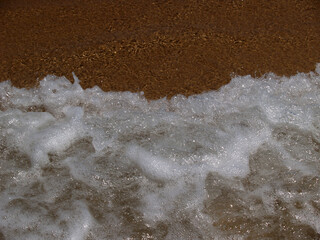 Waves crash onto the sandy shore, creating a burst of white foam. The dynamic movement and contrast capture the essence of the ocean's raw power and beauty.