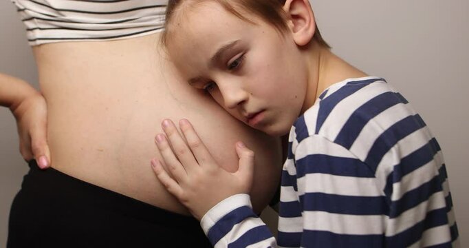 Little boy looking at her mother pregnant tummy. Pregnant mother and son spending time together at home. Pregnancy, family, parenthood, preparation and expectation concepts.