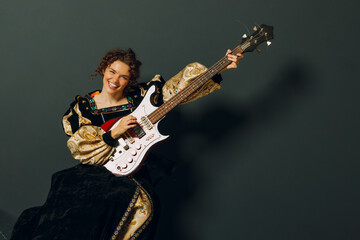 Portrait of a young adult woman playing music on electric guitar and dressed in a medieval dress