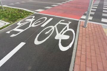 Bicycle path along sidewalk and lawn. Painted bike symbols on asphalt. Urban cycling route. Green space and pedestrian walkway. Ecologically friendly city.