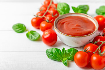Tomato paste, sauce, ketchup in a bowl and cherry tomatoes with fresh basil leaves on a textured wooden background. Vitamins and detox diet. Vegetable and vegetarian food. Space for text. Copy space.