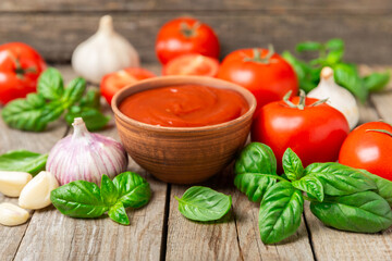 Tomato paste, sauce, ketchup in a bowl and cherry tomatoes with fresh basil leaves on a textured wooden background. Vitamins and detox diet. Vegetable and vegetarian food. Space for text. Copy space.