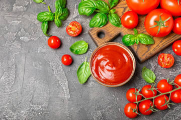 Tomato paste, sauce, ketchup in a bowl and cherry tomatoes with fresh basil leaves on a textured...