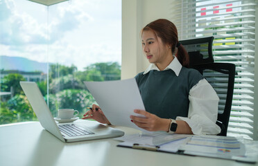 Beautiful young businesswoman looking at laptop screen, browsing internet or reading email from client.