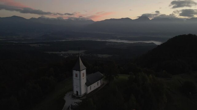 Aerial view of St. Primoz church at sunrise with Julian Alps peaks, Jamnik, Slovenia.