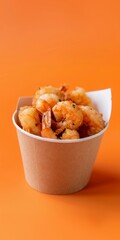 A paper cup filled with crispy fried shrimp, set against a vibrant orange background, highlighting a tasty seafood snack.